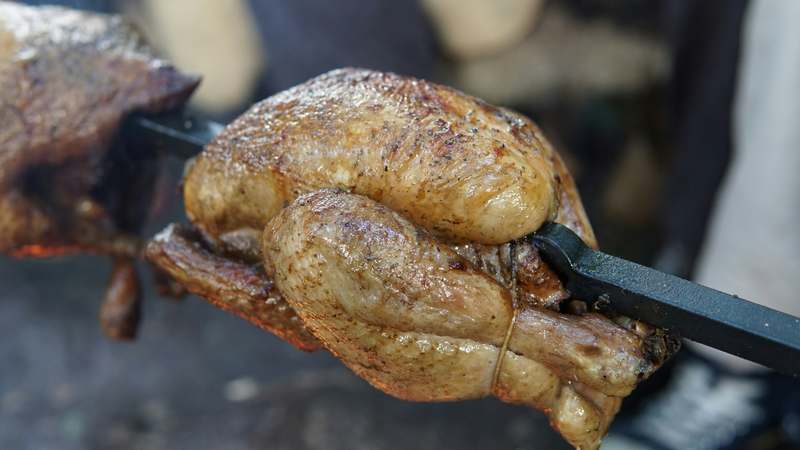 Stainless steel countertop rotisserie oven with rotating spit, herbs and roasted chicken visible, warm ambient lighting